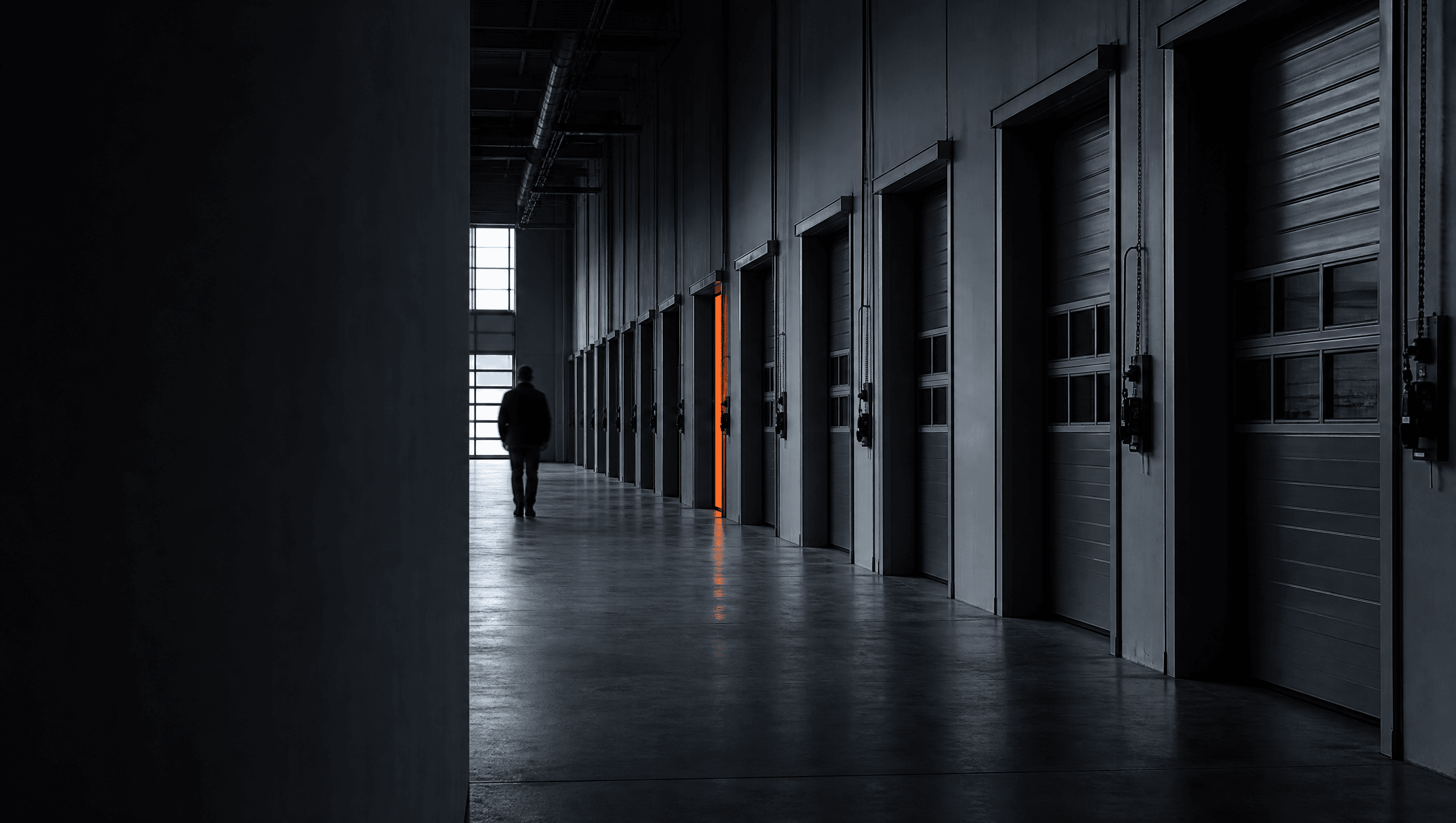 Una persona percorre il corridoio di un'officina con una porta illuminata di arancione